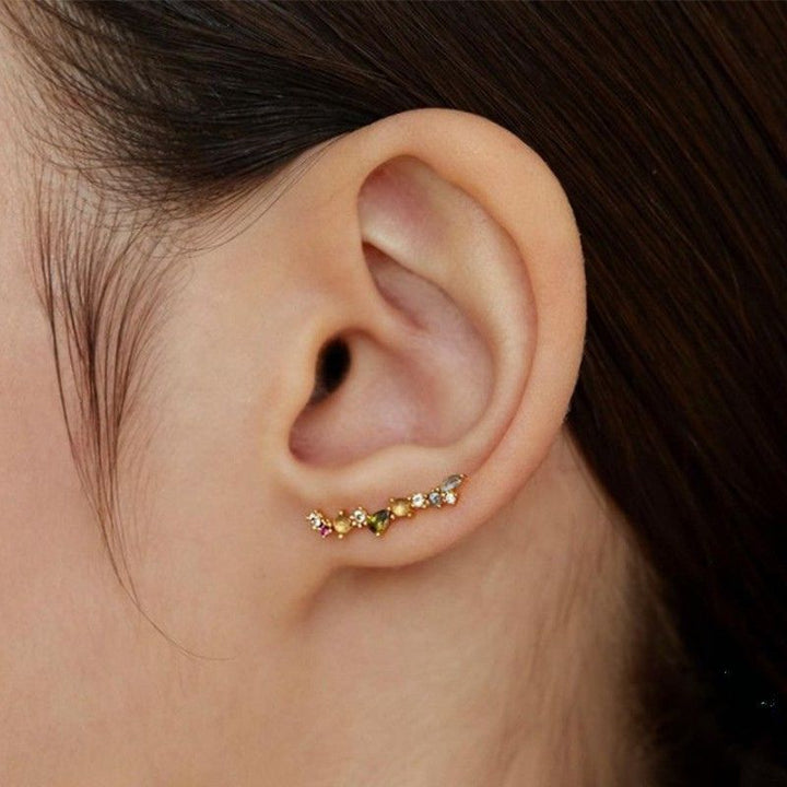 Close-up of an ear wearing a gold ear climber or crawler earring with small gemstones.