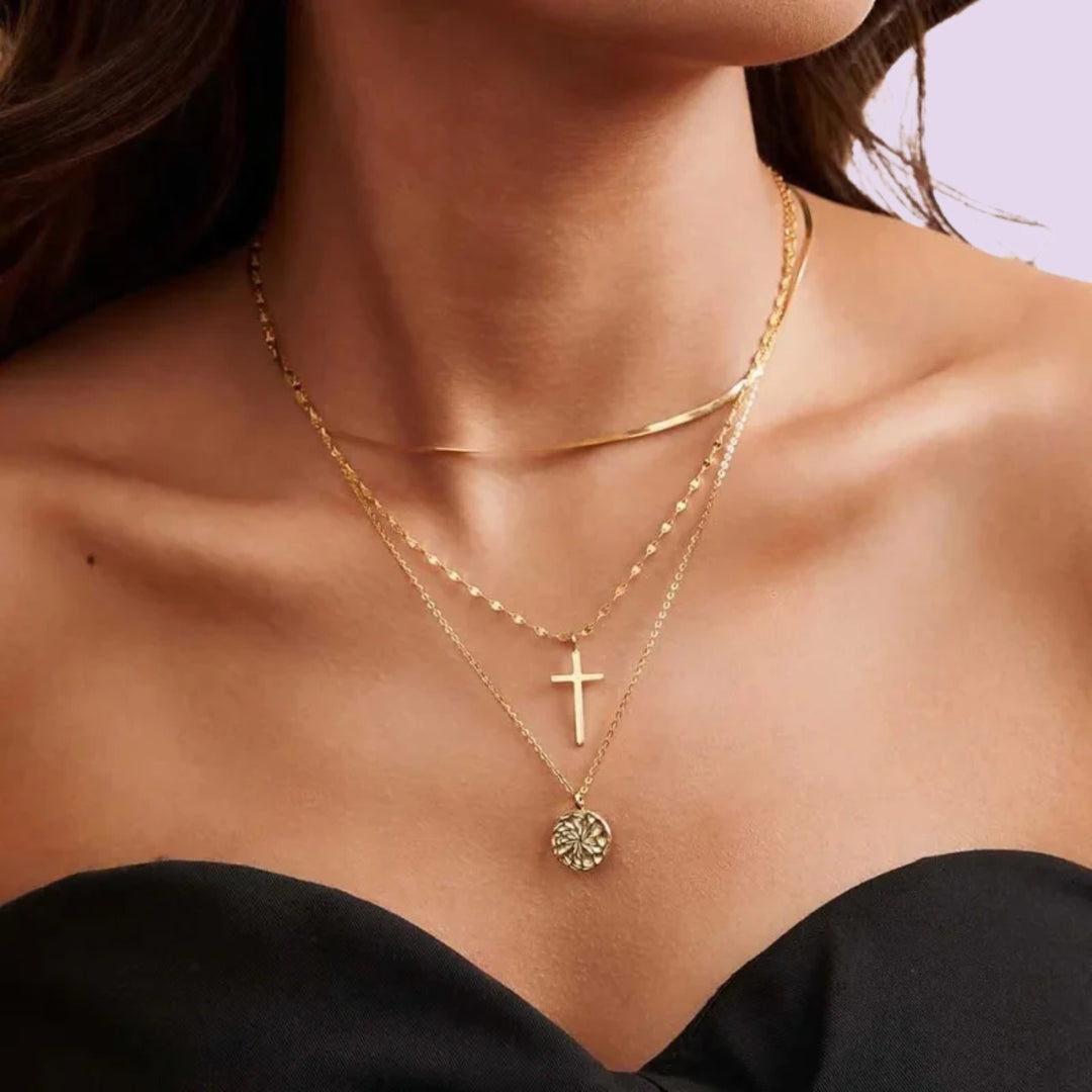 Gold layered necklace with a cross charm and round floral pendant worn over a black top