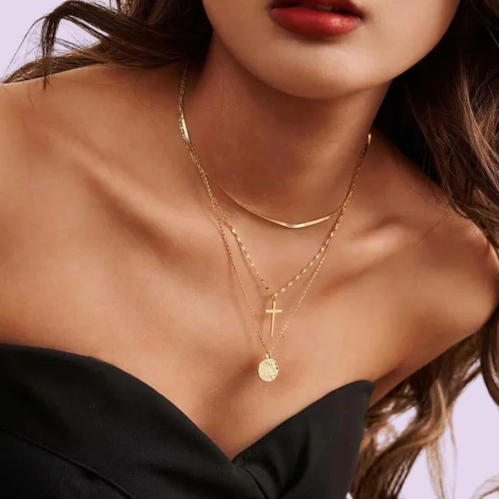 Gold layered necklace featuring a delicate cross pendant and round floral engraved pendant on a woman