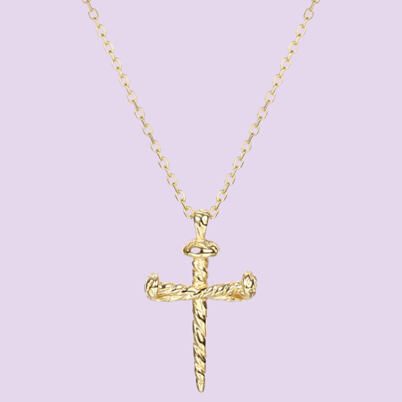 A gold chain necklace featuring a detailed cross nail pendant  set against a solid light purple background, 