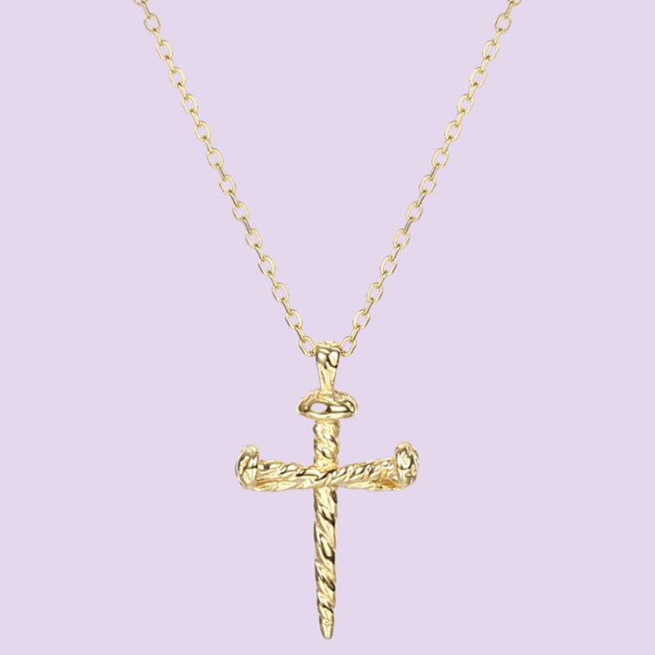 A gold chain necklace featuring a detailed cross nail pendant  set against a solid light purple background, 