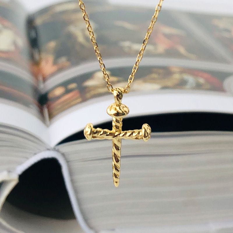 A gold cross nail pendant necklace with a twisted rope design hangs over an open book. 