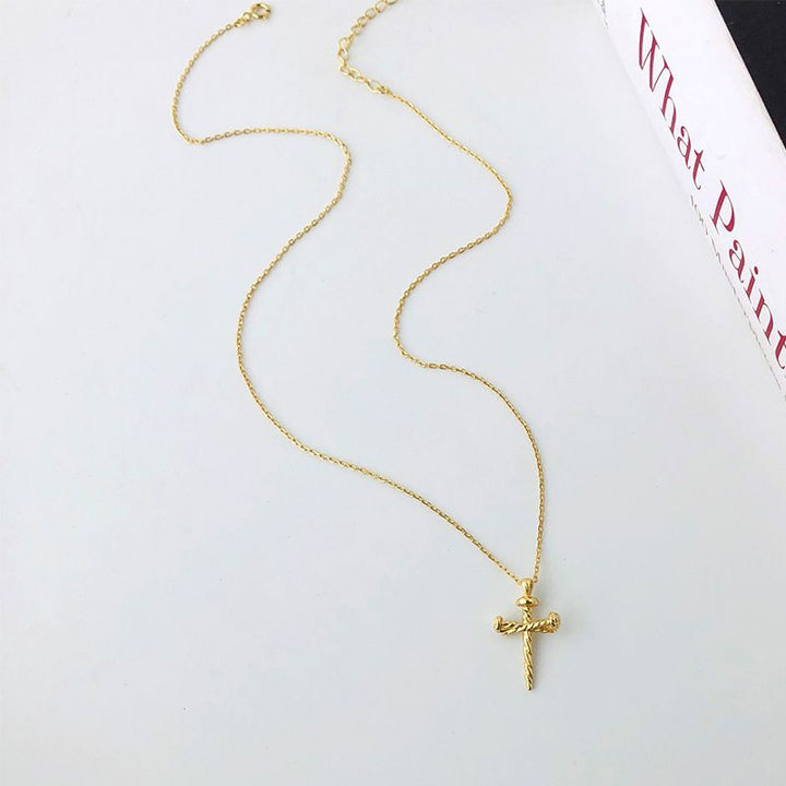 Gold necklace with a nail cross pendant on a white surface