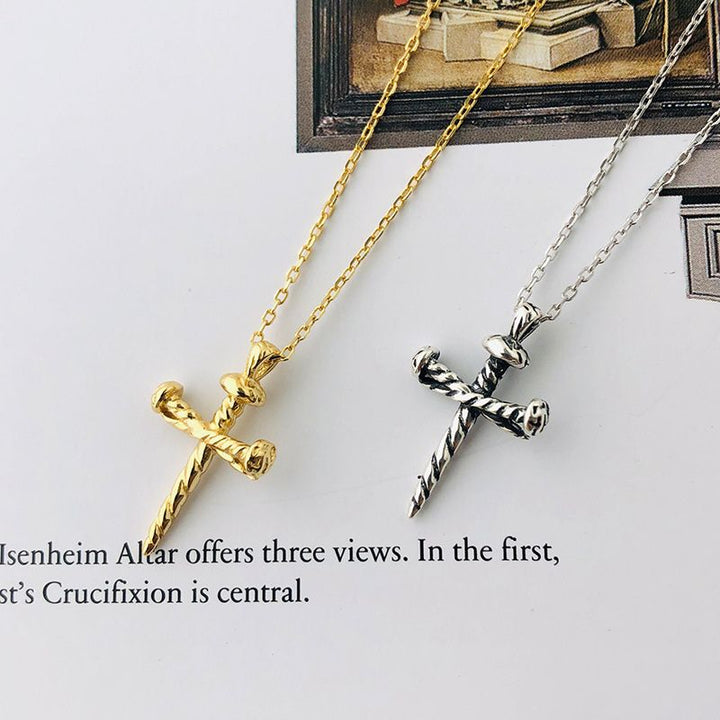 Two cross-shaped nail pendants on gold and silver chains against a light background.