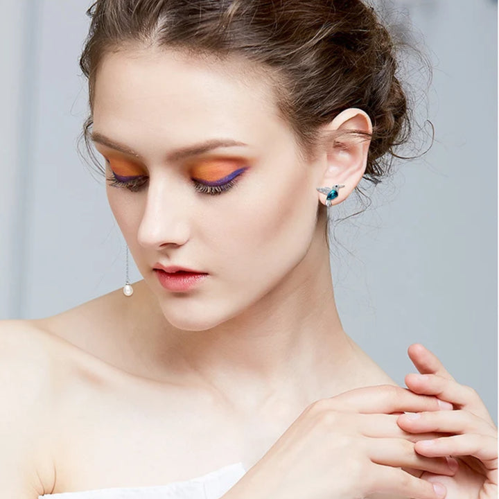Hummingbird asymmetrical earrings worn by a woman showing the mismatched stud and dangling pearl design