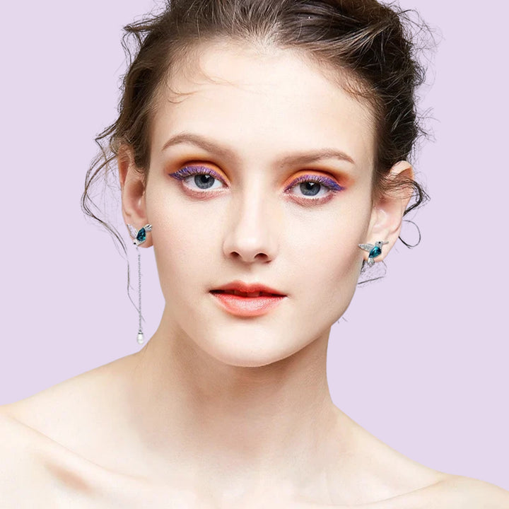 Hummingbird asymmetrical earrings worn by a woman showing the mismatched stud and dangling pearl design